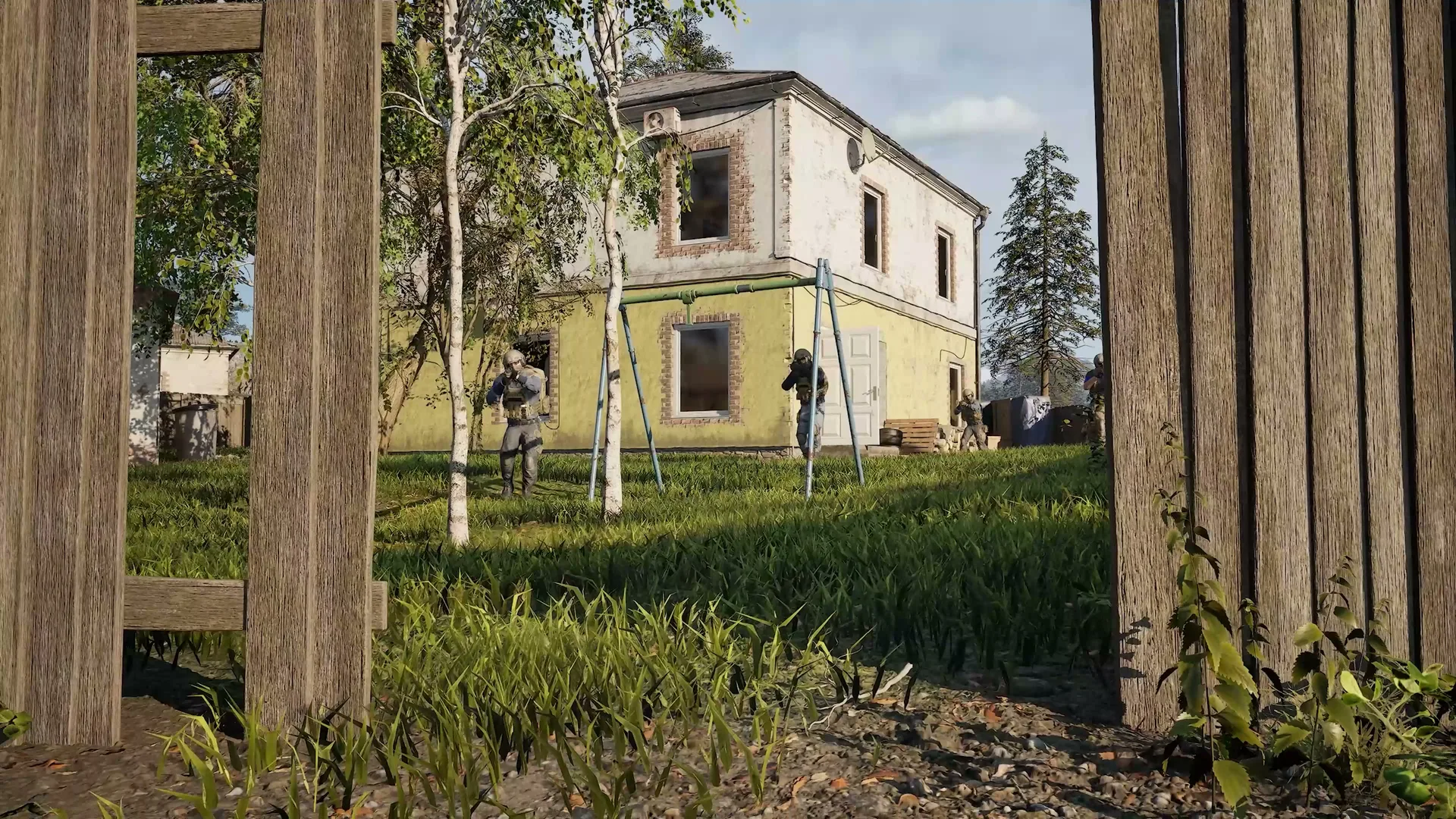 A squad approaches a yellow house beside trees in the WARDOGS reveal trailer.